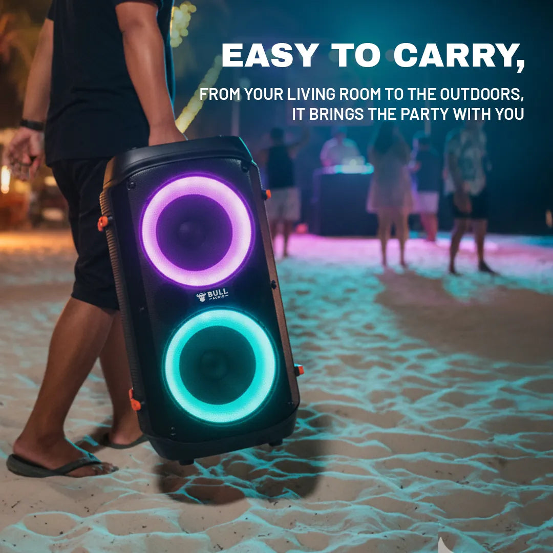 Bull Audio Alpha portable speaker with vibrant purple and teal LED lights carried on beach.